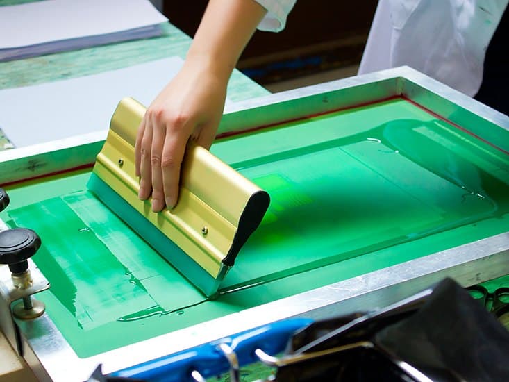 Dye being pulled across a mesh screen by hand, printing a length of cotton